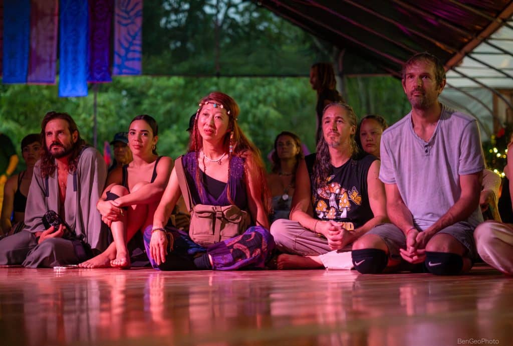 some young women and men sitting together on a wooden floor during a ceremonial part of a movement event